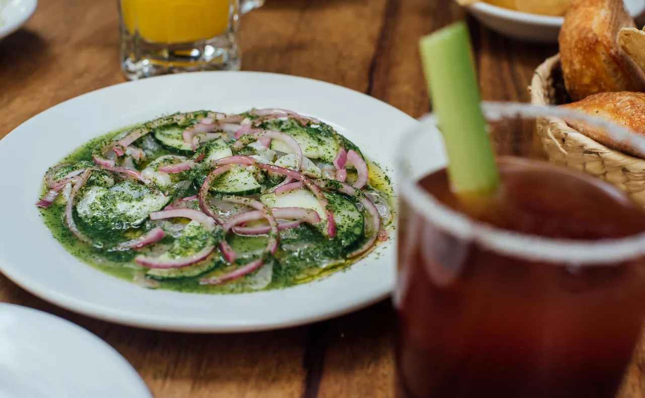 A green aguachile with red onion, beside a salt-rimmed drink.